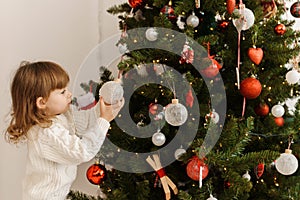 A cute little girl decorates the Christmas tree on Christmas morning.