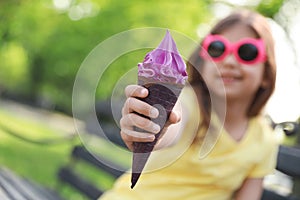Cute little girl with delicious ice cream on bench in park