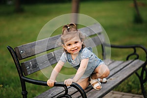 Cute little girl in denim climbs on the bench in the park. Happy smiled kid on the bench