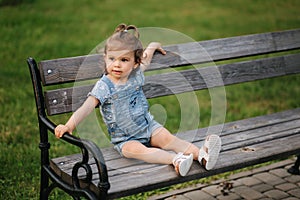 Cute little girl in denim climbs on the bench in the park. Happy smiled kid on the bench