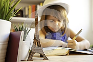 Cute little girl doing homework in her bedroom at the desk - Child girl writing in her diary imagining a trip to Paris - Childhood
