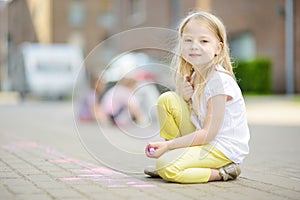 Cute little girl drawing with colorful chalks on a sidewalk. Summer activity for small kids.