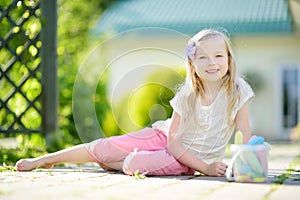 Cute little girl drawing with colorful chalks on a sidewalk. Summer activity for small kids.