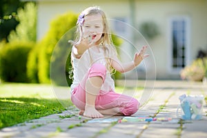 Cute little girl drawing with colorful chalks on a sidewalk. Summer activity for small kids.