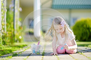 Cute little girl drawing with colorful chalks on a sidewalk. Summer activity for small kids.