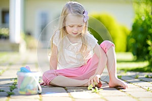 Cute little girl drawing with colorful chalks on a sidewalk. Summer activity for small kids.