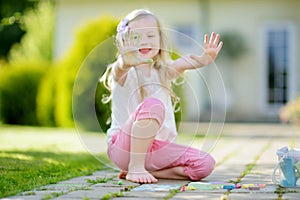 Cute little girl drawing with colorful chalks on a sidewalk. Summer activity for small kids.