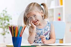 Cute little girl drawing with colorful pencils on paper. Pretty child painting indoors at home, daycare or kindergarten