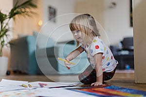Cute little girl drawing with crayons, sitting on the floor at home.