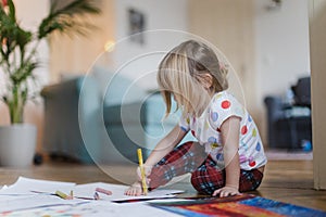 Cute little girl drawing with crayons, sitting on the floor at home.