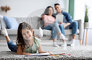 Cute Little Girl Drawing On Floor While Her Parents Relaxing On Couch