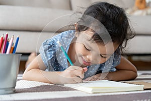 Cute little girl drawing homework and writing with pen on paper in her home