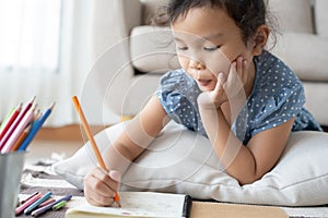 Cute little girl drawing homework and writing with pen on paper in her home