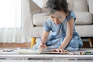 Cute little girl drawing homework and writing with pen on paper in her home