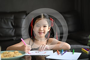 Cute little girl drawing on paper with colored pencils in living room