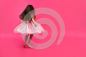 Cute little girl dreams of becoming a ballerina. Little Dancing Girl. Studio Shoot Over Pink Background