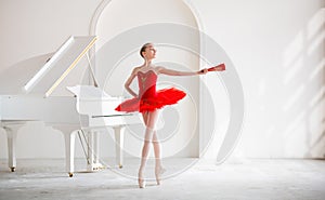 A cute little girl dreams of becoming a professional ballerina. In a white room, next to the piano, a girl in a bright red tutu