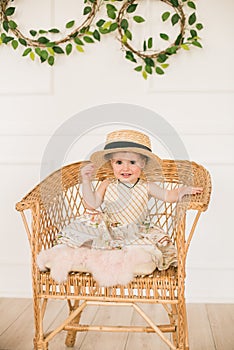 Cute little girl in a dress with a floral print and a straw hat is a boater in Easter scenery in the studio