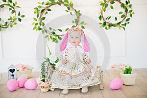 Cute little girl in a dress with a flower print and a bunny hat in the Easter decorations in the studio.