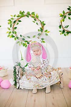 Cute little girl in a dress with a flower print and a bunny hat in the Easter decorations in the studio.