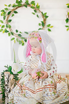 Cute little girl in a dress with a flower print and a bunny hat in the Easter decorations in the studio.
