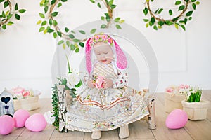 Cute little girl in a dress with a flower print and a bunny hat in the Easter decorations in the studio.