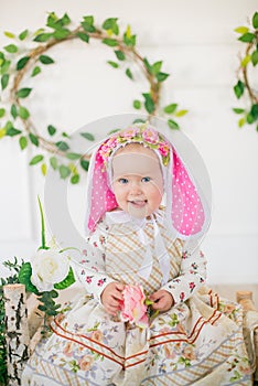 Cute little girl in a dress with a flower print and a bunny hat in the Easter decorations in the studio.