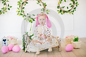 Cute little girl in a dress with a flower print and a bunny hat in the Easter decorations in the studio.