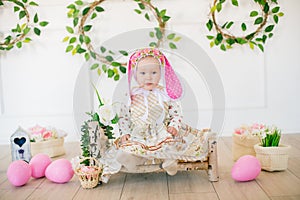 Cute little girl in a dress with a flower print and a bunny hat in the Easter decorations in the studio.