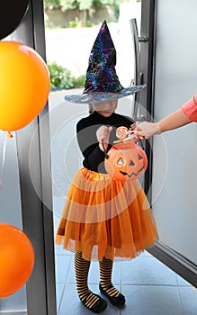 Cute little girl dressed as witch trick-or-treating at doorway