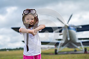 A cute little girl dressed in a cap and glasses of a pilot on the background of an airplane. The child dreams of