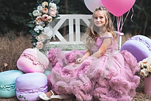 Cute little girl dressed in pink stunning dress holds French Macaron