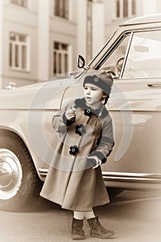 Cute little girl dressed in retro coat posing near oldtimer car