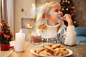 Cute little girl drinking cacao and eating cookie at home