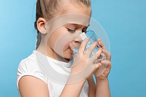 Cute little girl drinking fresh water from glass on light blue background