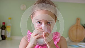 Cute little girl drinking a glass of milk in the kitchen at home. Slow motion little girl drinking water. Close-up. The