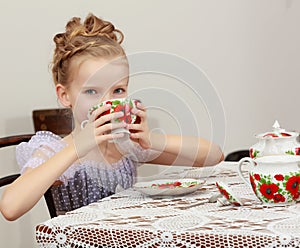 Cute little girl drinking tea at the old table.