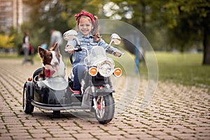 Cute little girl  driving electrical motorcycle toy with sidecar and her dog in it