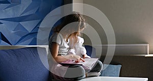 Cute little girl eading a book with stuffed teddy bunny toy