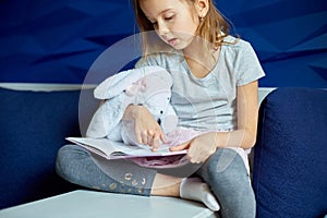 Cute little girl eading a book with stuffed teddy bunny toy