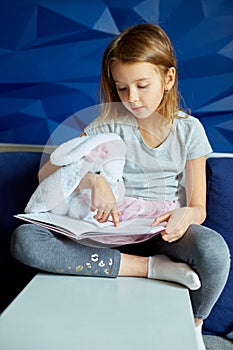 Cute little girl eading a book with stuffed teddy bunny toy