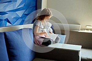 Cute little girl eading a book with stuffed teddy bunny toy