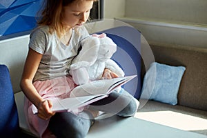 Cute little girl eading a book with stuffed teddy bunny toy photo