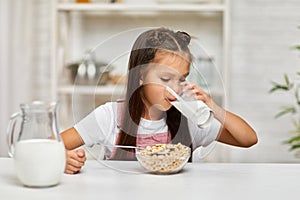 Cute little girl eating breakfast: cereal with the milk