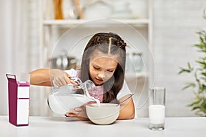 Cute little girl eating breakfast: cereal with the milk