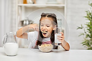 Cute little girl eating breakfast: cereal with the milk