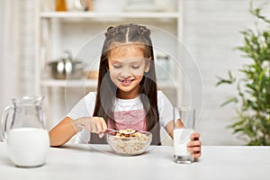 Cute little girl eating breakfast: cereal with the milk