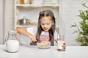 Cute little girl eating breakfast: cereal with the milk