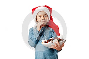 Cute little girl eating candy for christmas and new year. Portrait of a child in a Santa hat, isolated on a white background