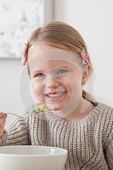 Cute little girl eating a fruit salad in design dining room. Child having a dinner at home. Healthy nutrition for small